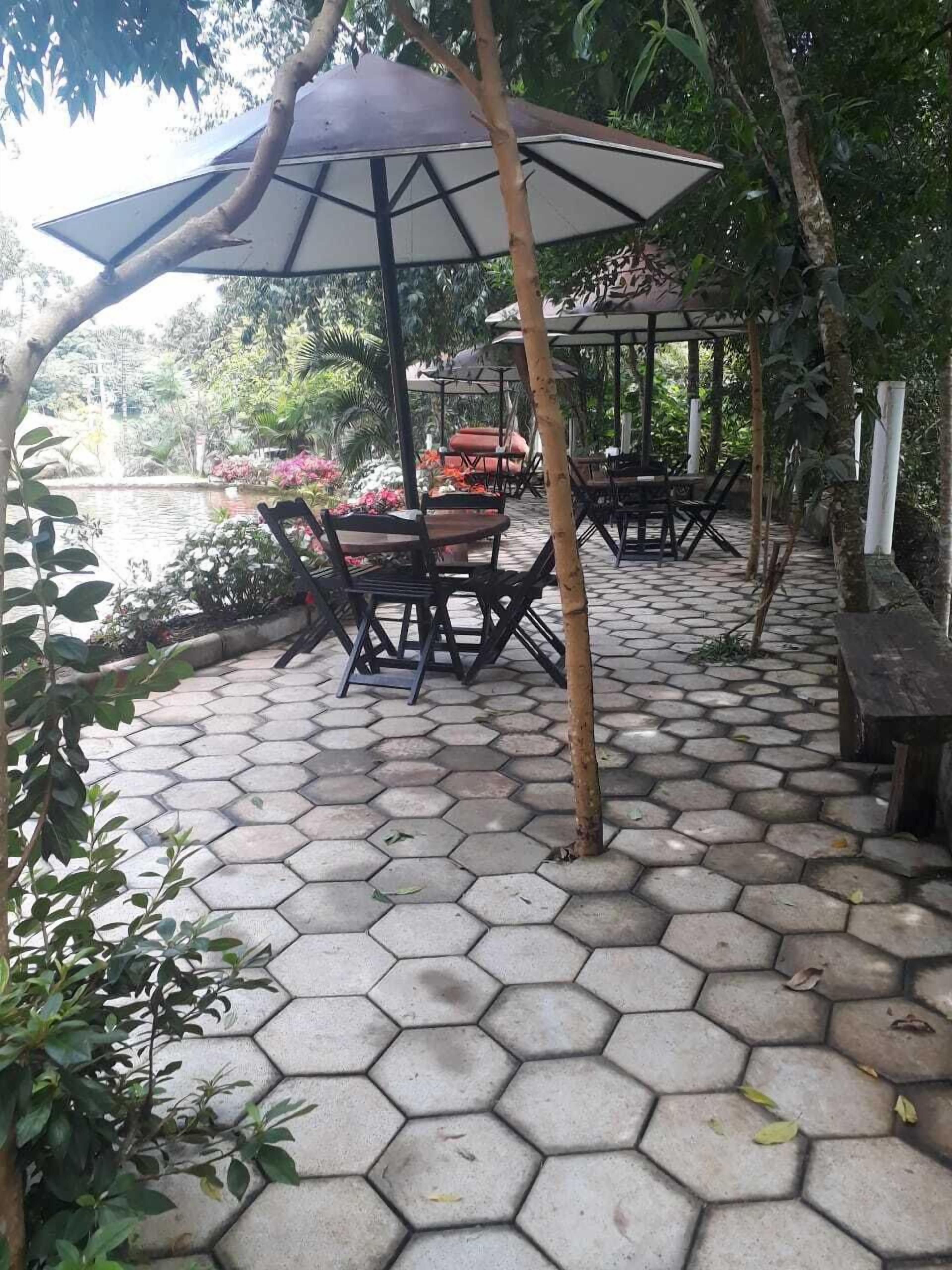 A hexagonal tiled patio area with outdoor seating under a gazebo, surrounded by lush greenery and a view of a body of water.