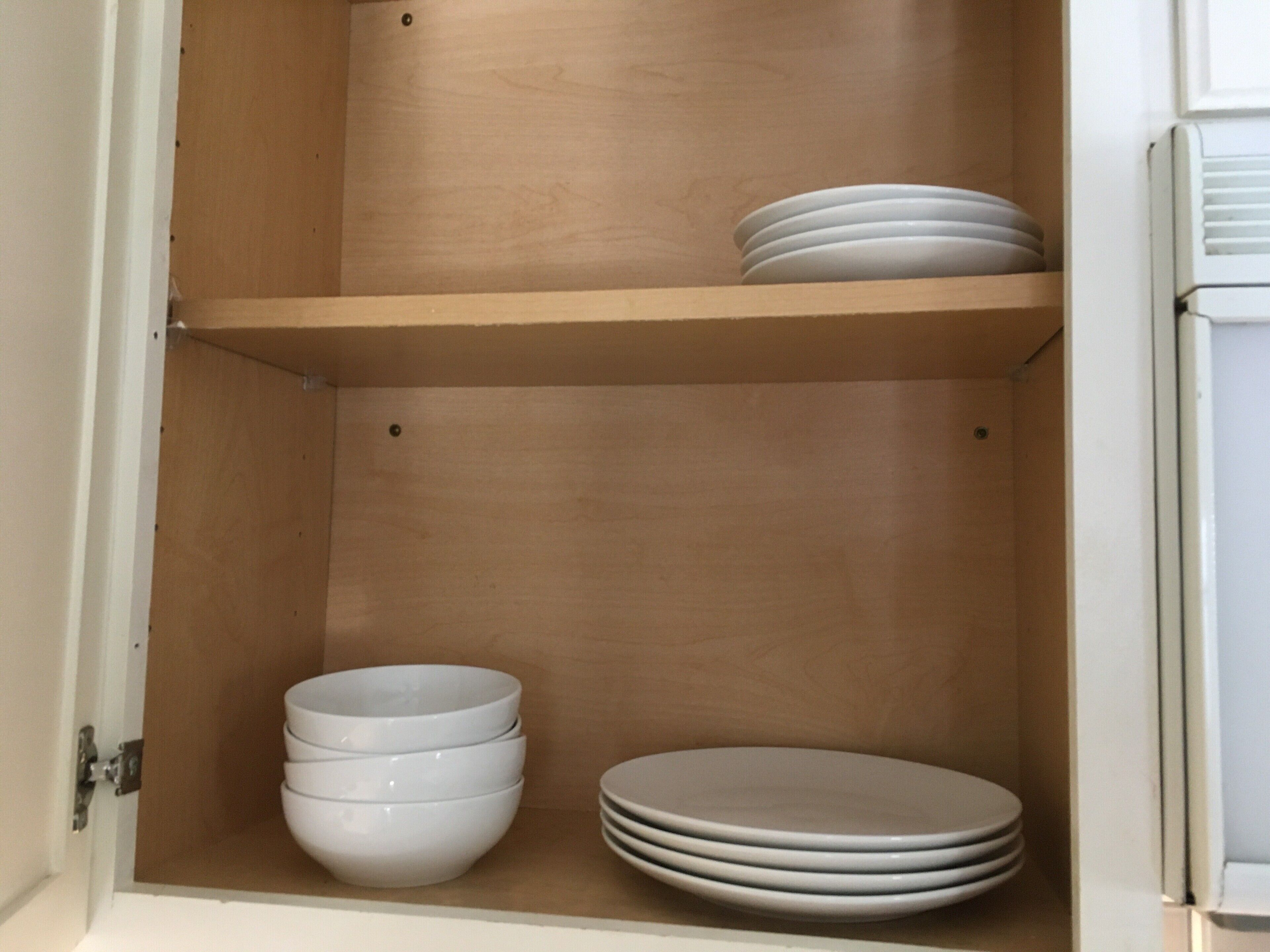 Un meuble en bois doté d’étagères, contenant des bols et des assiettes blancs.