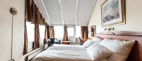 Una habitación de hotel con una cama grande, un escritorio, una silla y un ventanal con cortinas.