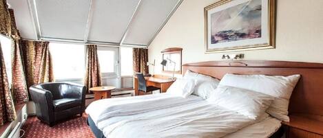 A hotel room with a large bed, a desk, a chair, and a window with curtains.