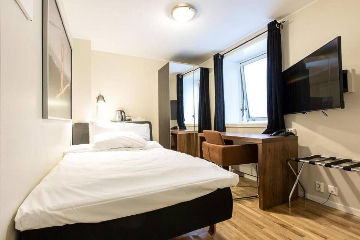 A hotel room with a bed, desk, chair, TV, and a window with curtains.