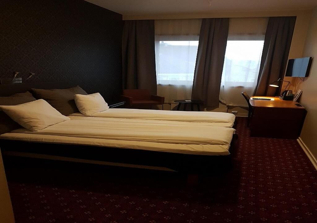 Habitación de hotel con cama doble, escritorio con silla, televisor y una mesita.