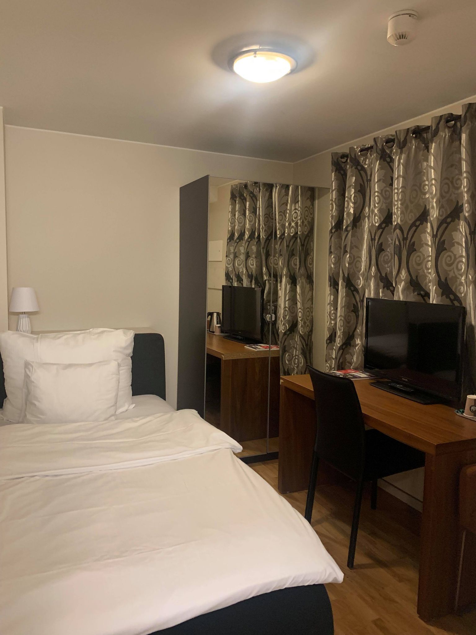 Habitación de hotel con cama, escritorio, silla, televisor y cortina estampada.