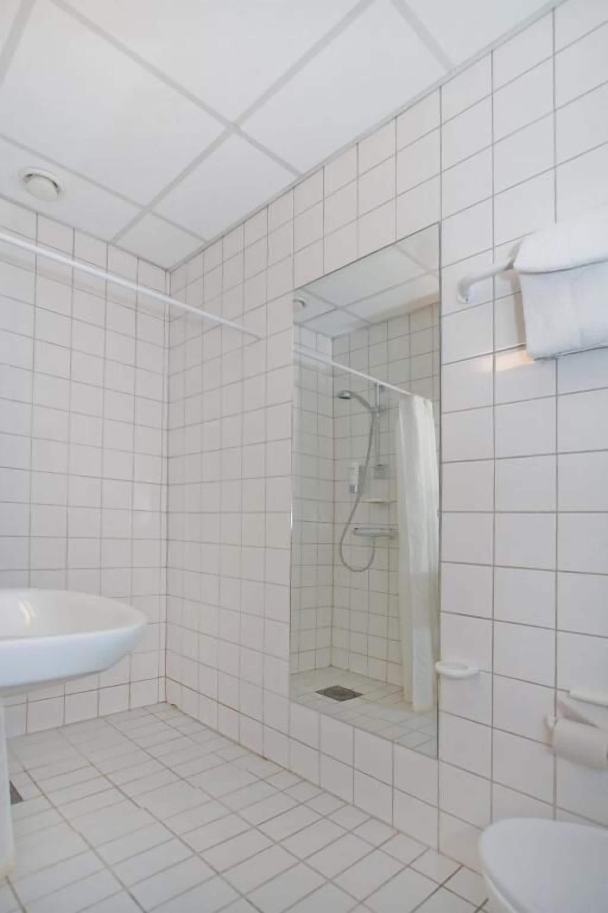 A bathroom with white tiles, a glass shower enclosure, a white sink, and a toilet.