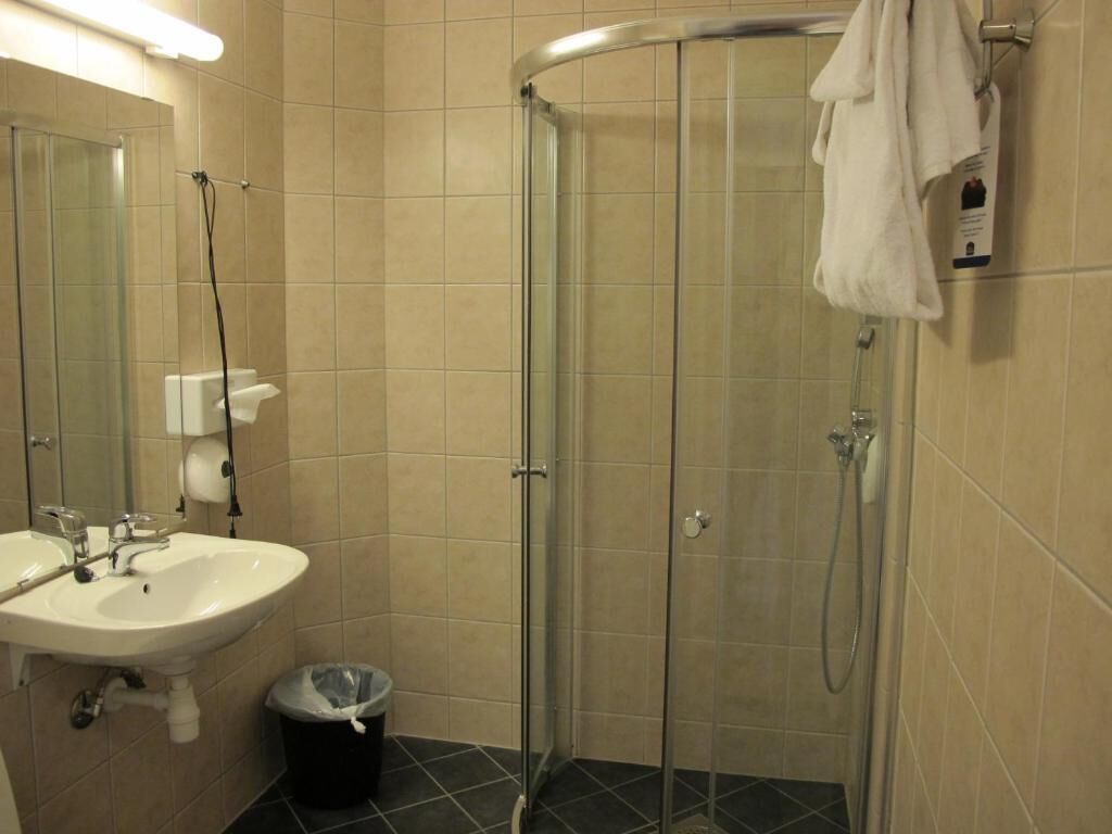 A bathroom with a glass-enclosed shower, a sink, and a trash bin.