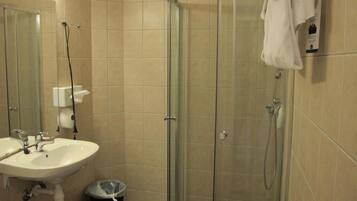 A bathroom with a glass-enclosed shower, a sink, and a trash bin.