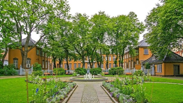 A courtyard with a central fountain, surrounded by a brick building with multiple windows and a well-maintained lawn. - Chesterfield Hotel (Trondheim)