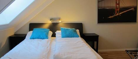 A bedroom with a large bed, two nightstands, a skylight, and a painting of a bridge.