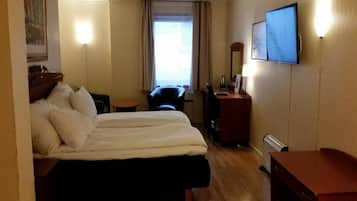 A hotel room with a double bed, a desk with a chair, a TV mounted on the wall, and a window with curtains.