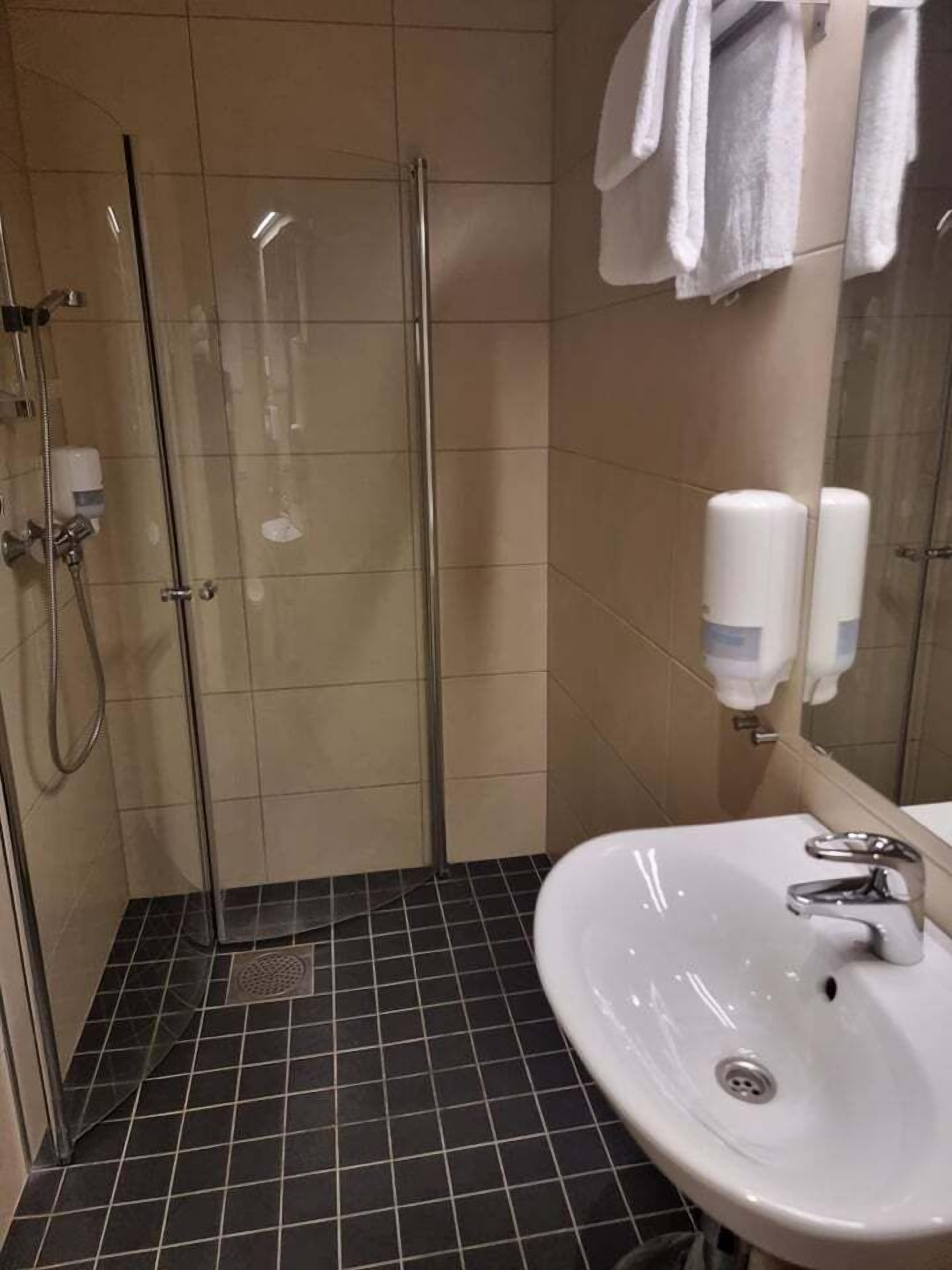 A bathroom with a glass shower enclosure, a sink with a mirror, and two hand soap dispensers.