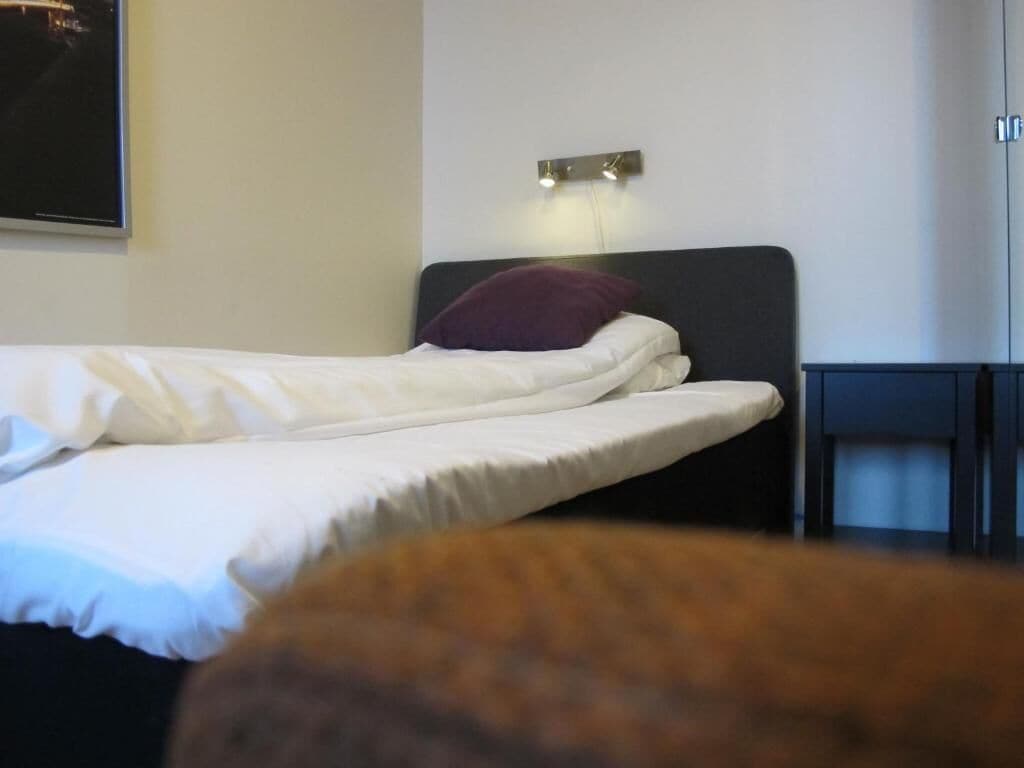 A neatly made bed with white linens and a purple pillow in a hotel room.
