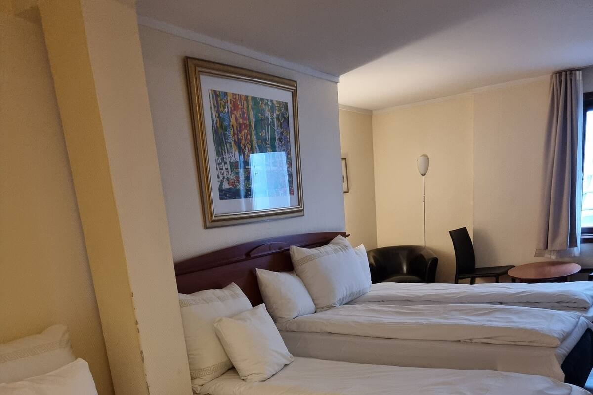 A hotel room with three single beds, a desk, a chair, and a framed picture on the wall.