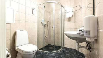 Un baño con ducha acristalada, inodoro y lavamanos con dispensador de jabón.