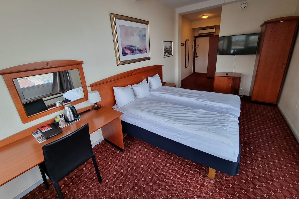 A hotel room with a large bed, a desk with a chair, a mirror, and a TV.