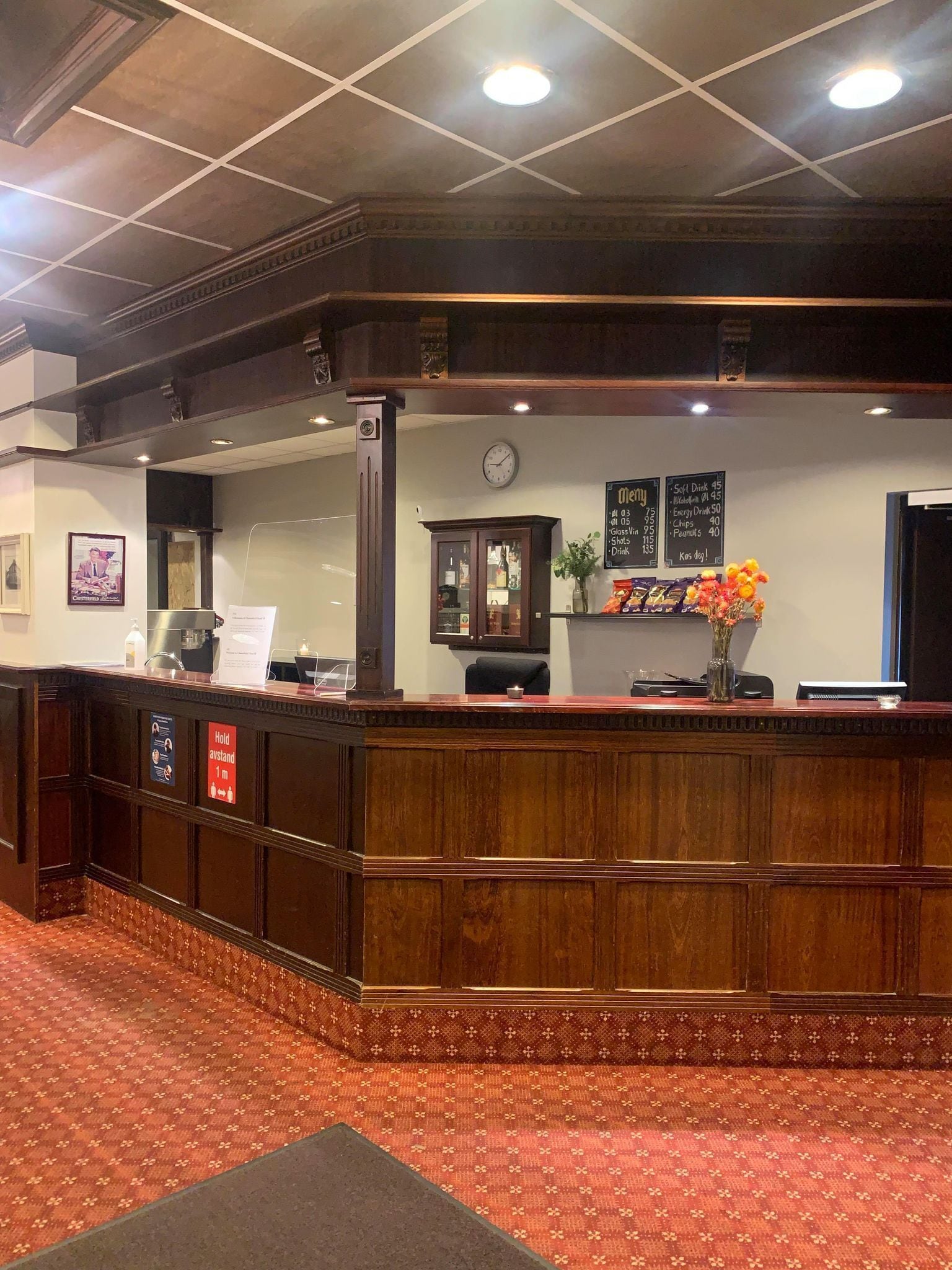 A reception area with a wooden counter, a clock, a menu board, and a small plant.