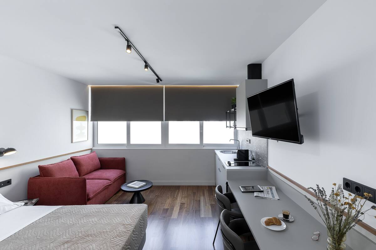 A modern, compact living space with a sofa, a dining area, a flat-screen TV, and a small kitchenette.