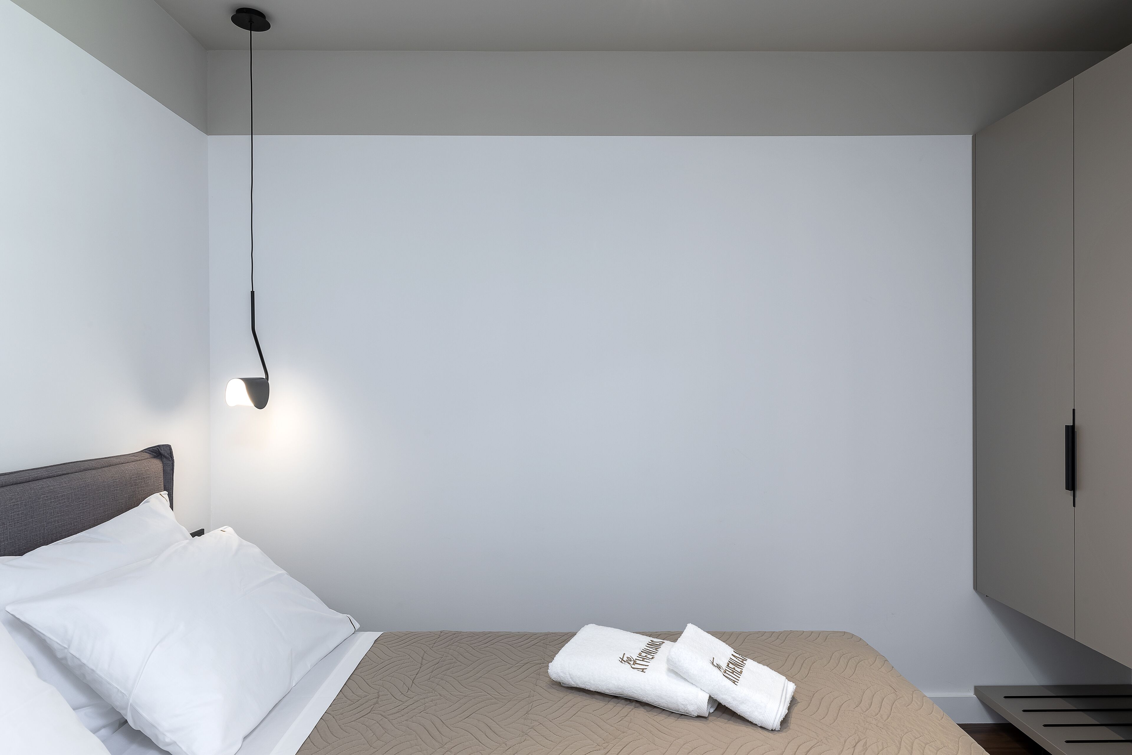 A minimalist bedroom with a bed, a wall-mounted light, and a wardrobe.