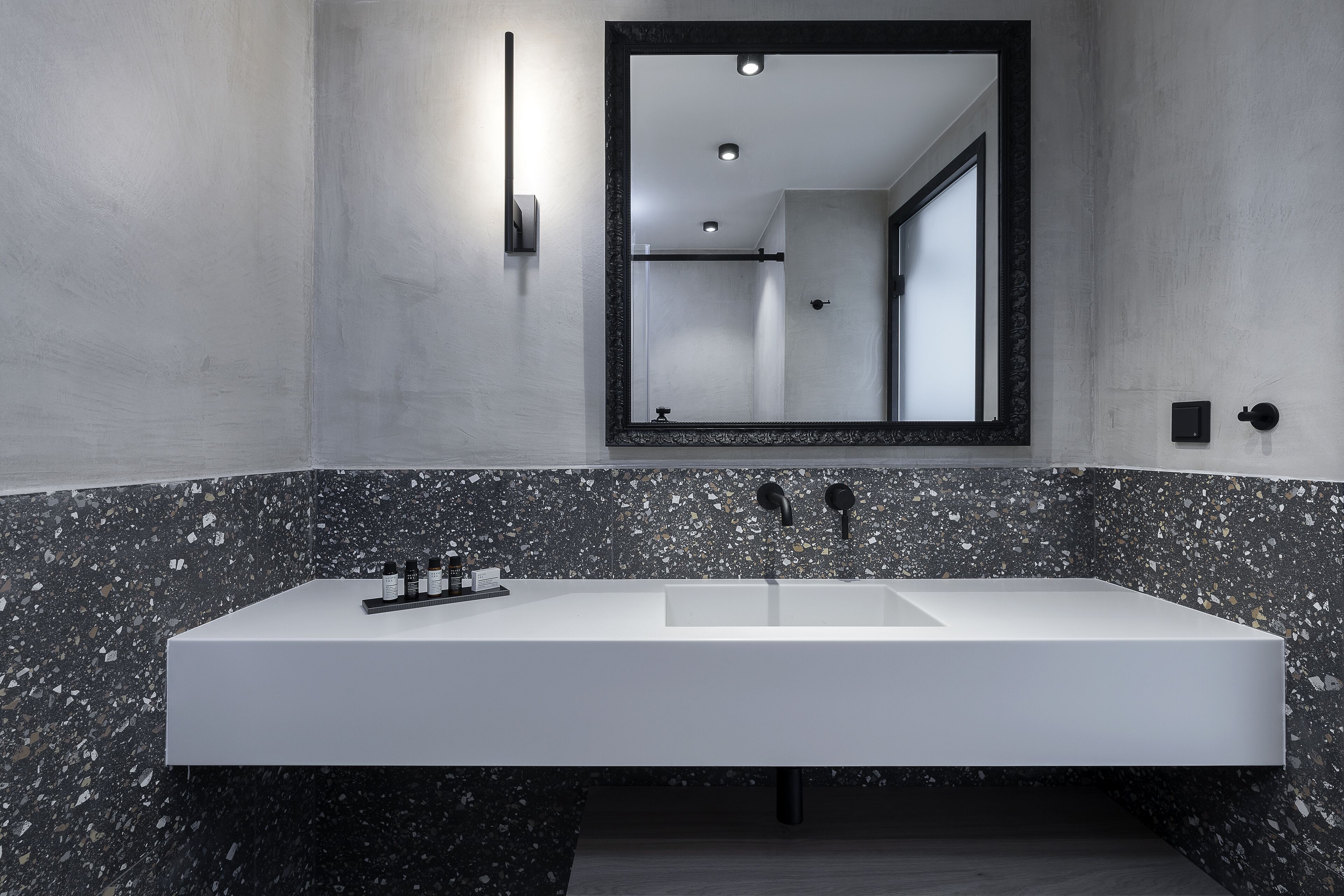 A modern bathroom with a large rectangular sink, a wall-mounted mirror, and a dark speckled tile backsplash.