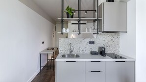 Una cuina moderna amb taulell blanc, rentamicroones d'acer inoxidable i armaris negres. Hi ha una planta sobre una estanteta a sobre del rentamicroones i una cafetera sobre el taulell.