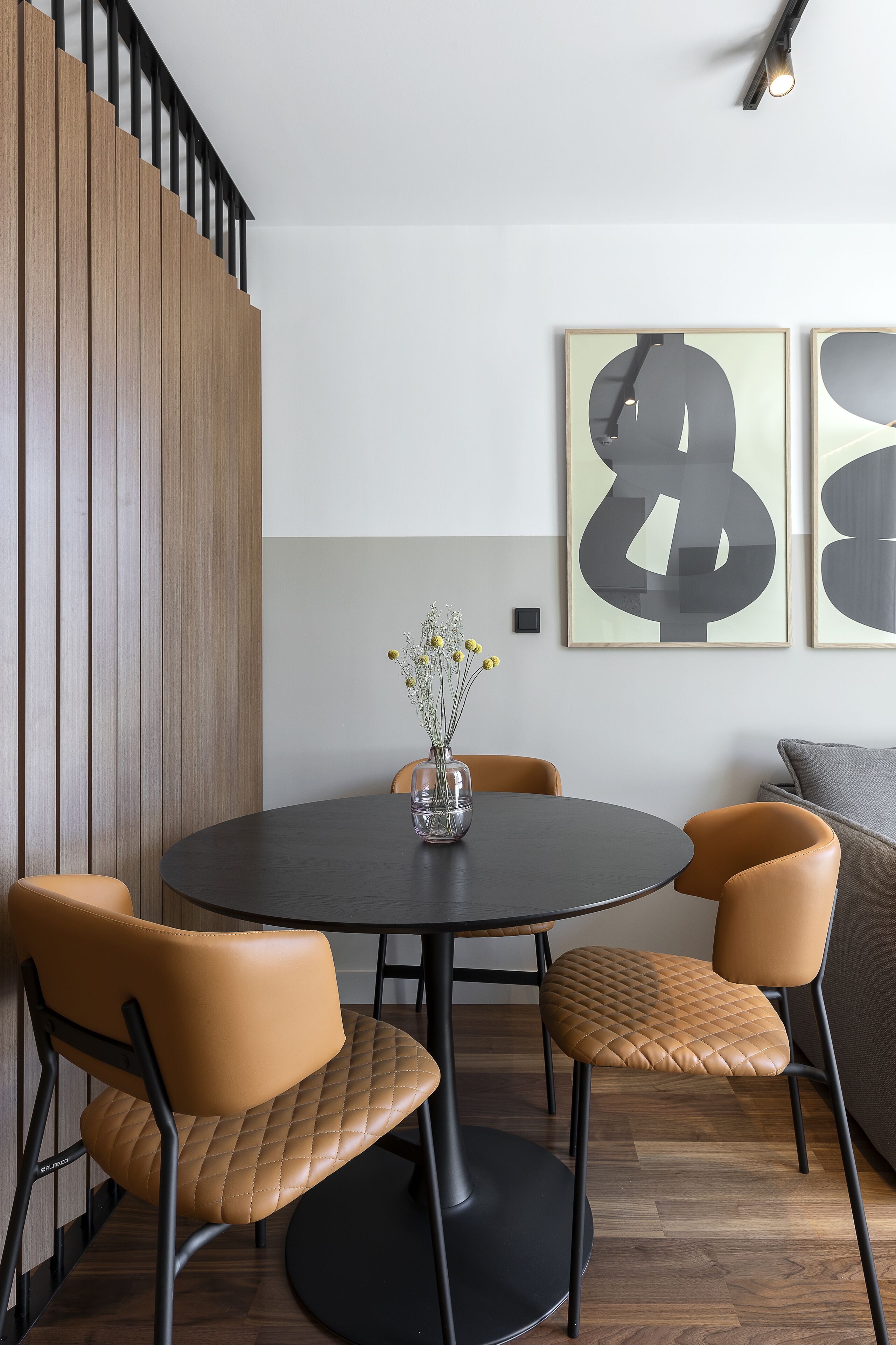 A modern dining area with a round table, four chairs, and abstract artwork on the wall.