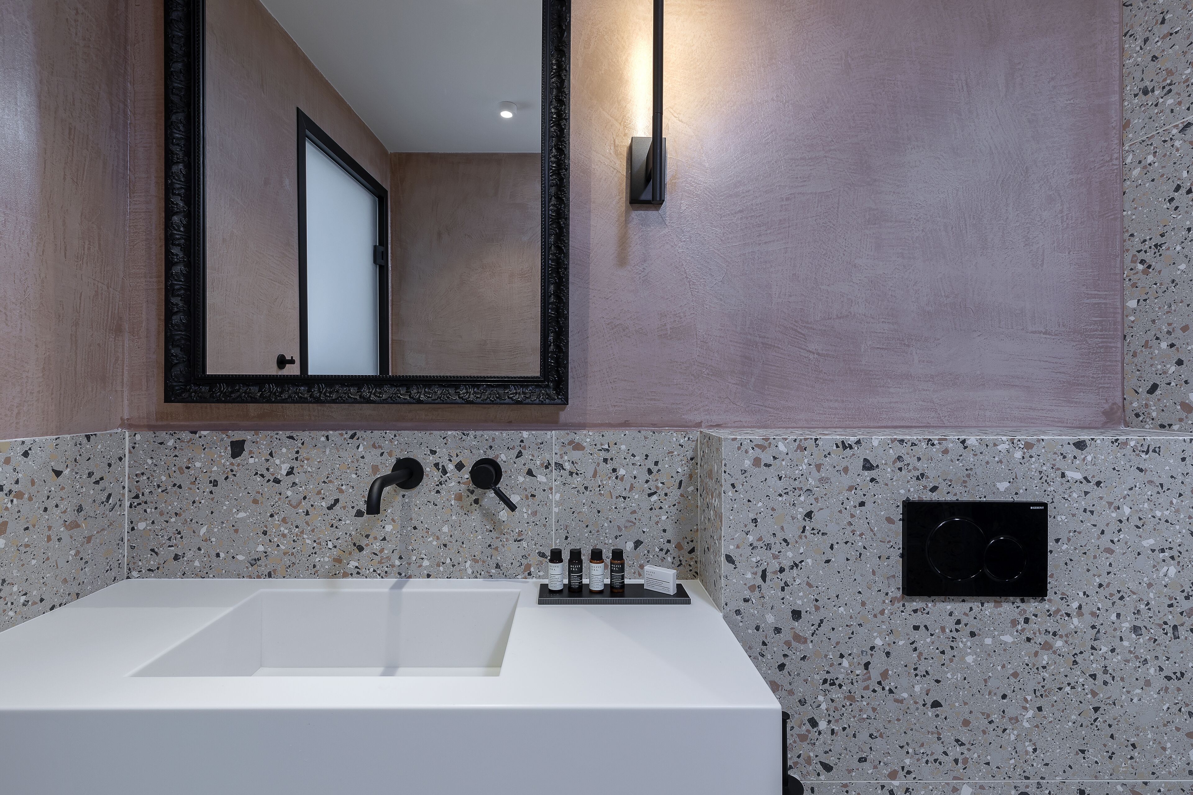 Une salle de bain moderne avec un grand lavabo blanc, un miroir et un pare-feu en carreaux à motifs.