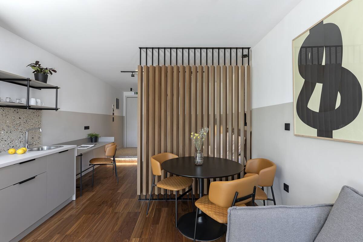 A modern kitchen with a white countertop, a sink, and a potted plant. There is a dining area with a round table and four chairs.