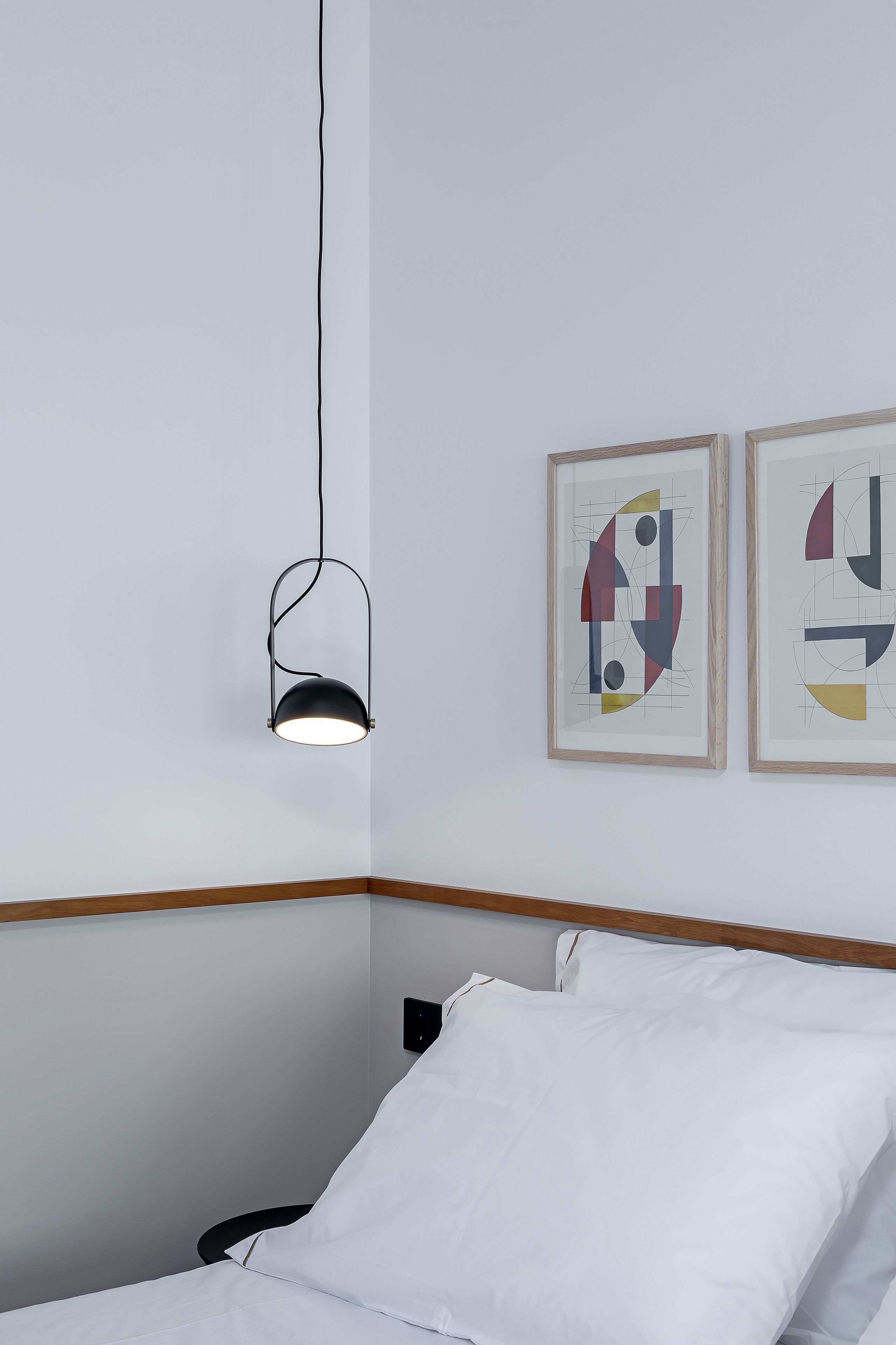 Una habitación minimalista con una cama, una lámpara colgante y dos obras de arte abstracto en la pared.