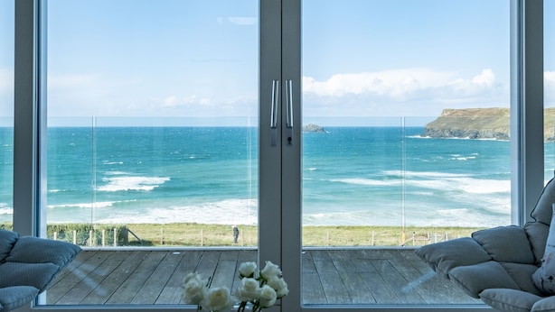 Une pièce dotée d’une grande porte vitrée donnant sur un balcon d’où l’on peut admirer l’océan et une côte rocheuse.