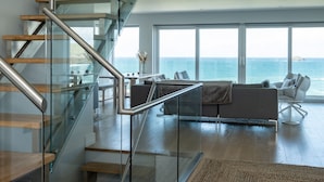 Un intérieur moderne avec un escalier en verre, un espace de vie offrant une vue sur l’océan et un coin repas avec une table et des chaises.