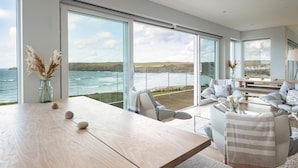 Un salon moderne doté d’une grande table en bois, de sièges confortables et de larges fenêtres offrant une vue imprenable sur la mer.