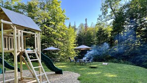 A playground with a slide and climbing structure, surrounded by a grassy area with picnic tables and umbrellas. - Large family & pet friendly home! Huge outdoor playset, backyard games & more!  (Wilmington)