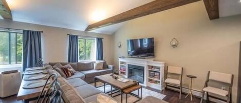 A modern living room with a sofa set, a dining table with chairs, a fireplace, and a television.