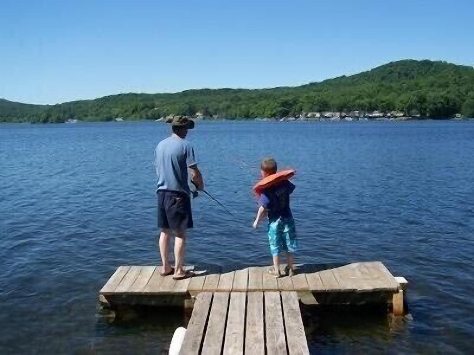 A wooden dock extending into a lake with a person and a child standing on it.