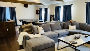 A modern living room with a grey sectional sofa, a coffee table, and a dartboard. - Large family & pet friendly home! Huge outdoor playset, backyard games & more!  (Wilmington)