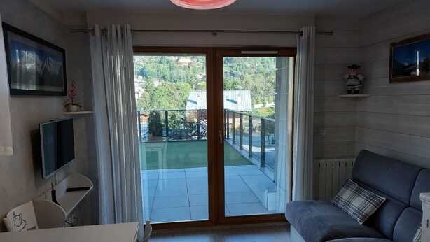 A living room with a sofa, a TV, a table, and a balcony with a view of greenery and buildings. - 200 m from the Saint Gervais les Bains cable car  (Saint-Gervais-les-Bains)