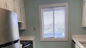 A kitchen with white cabinets, a stainless steel refrigerator, a stove, and a window with blinds. - Just bring your bathing suit ! Steps to the beach ! (Myrtle Beach)