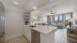 Uma cozinha moderna com armários brancos, uma ilha grande com pia e um espaço de refeições com cadeiras azul-claras.