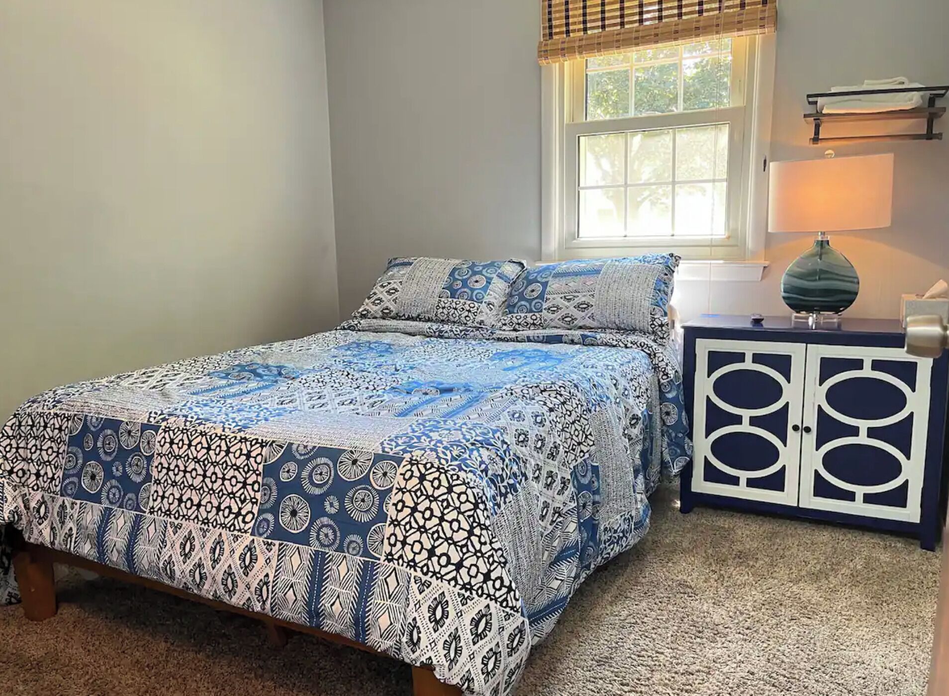 A bedroom with a bed, a nightstand, a lamp, and a window with blinds.