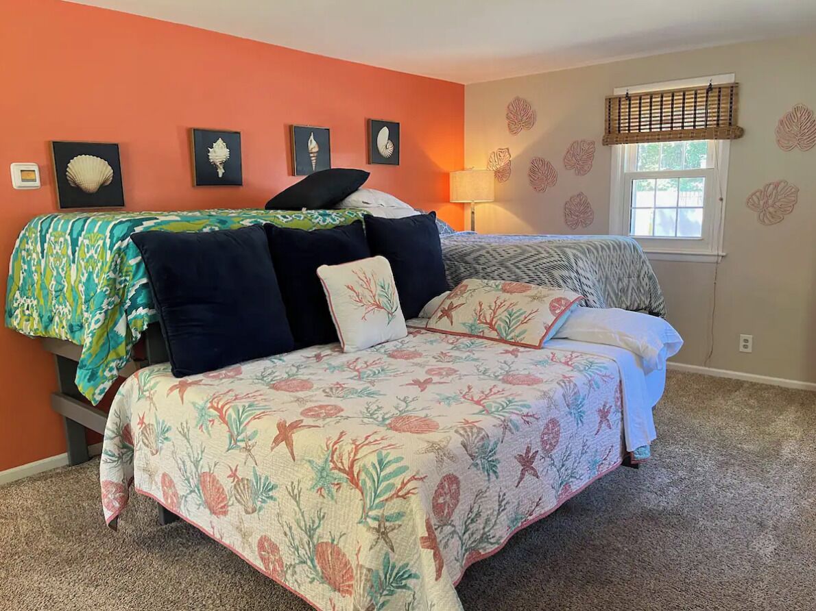 A bedroom with a bed, two pillows, a nightstand, a lamp, and wall art.