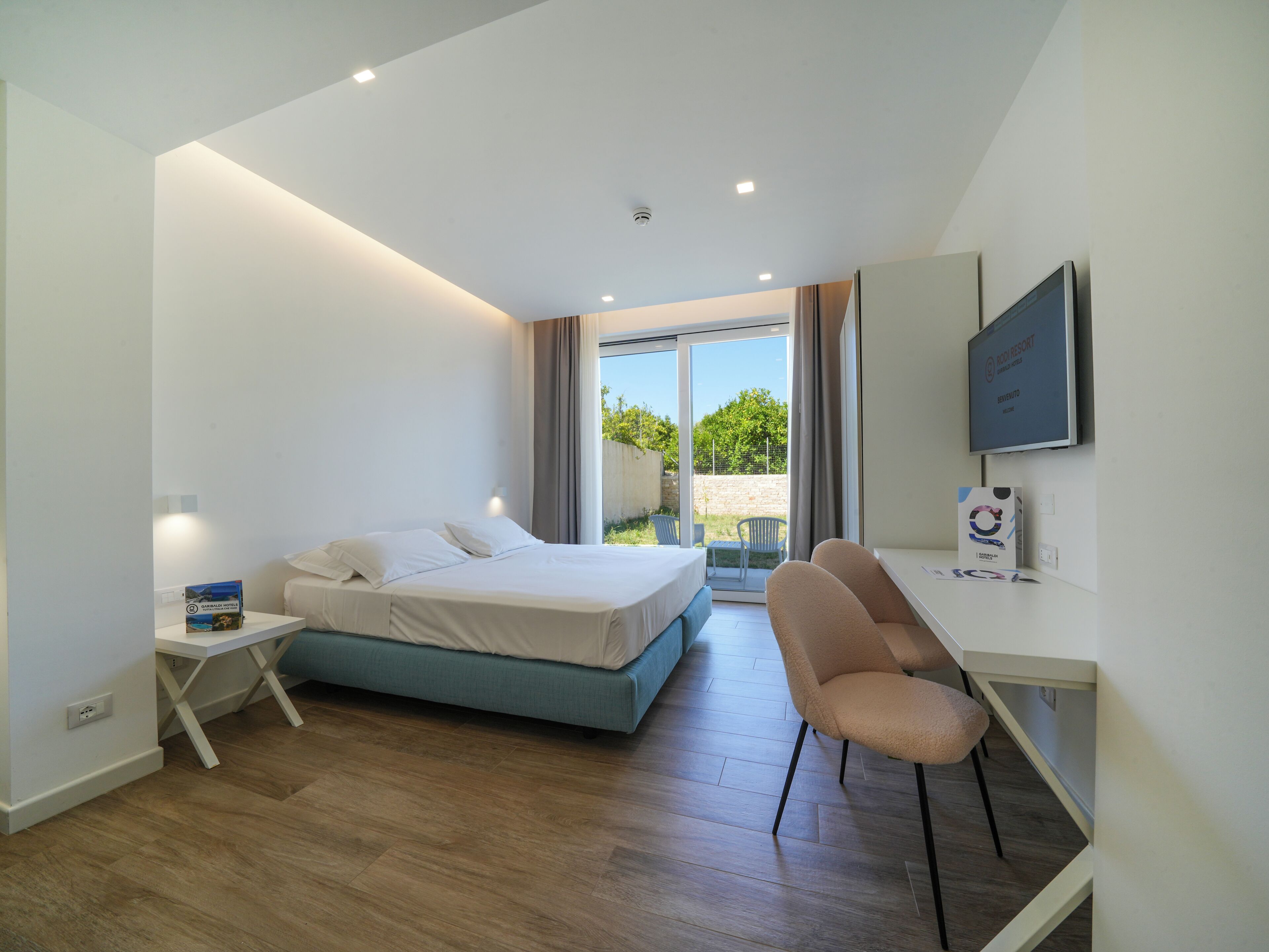 Una habitación de hotel moderna con una cama, un escritorio, una silla, un televisor y vistas al exterior.