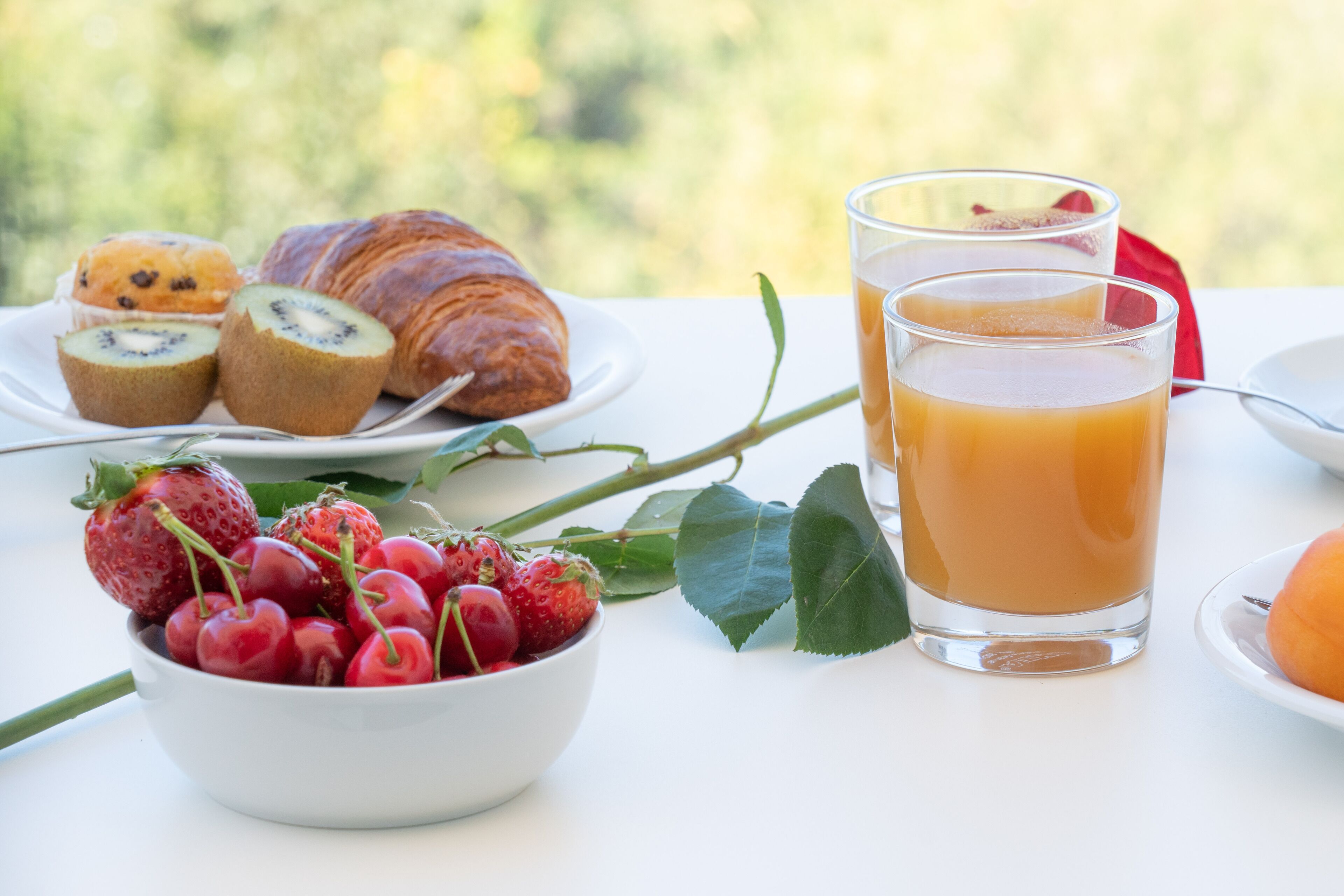 A table with a croissant, kiwi slices, a bowl of cherries, and a glass of orange juice.
