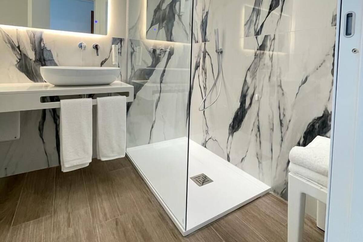 A modern bathroom with a glass-enclosed shower, a marble vanity, and a large mirror.