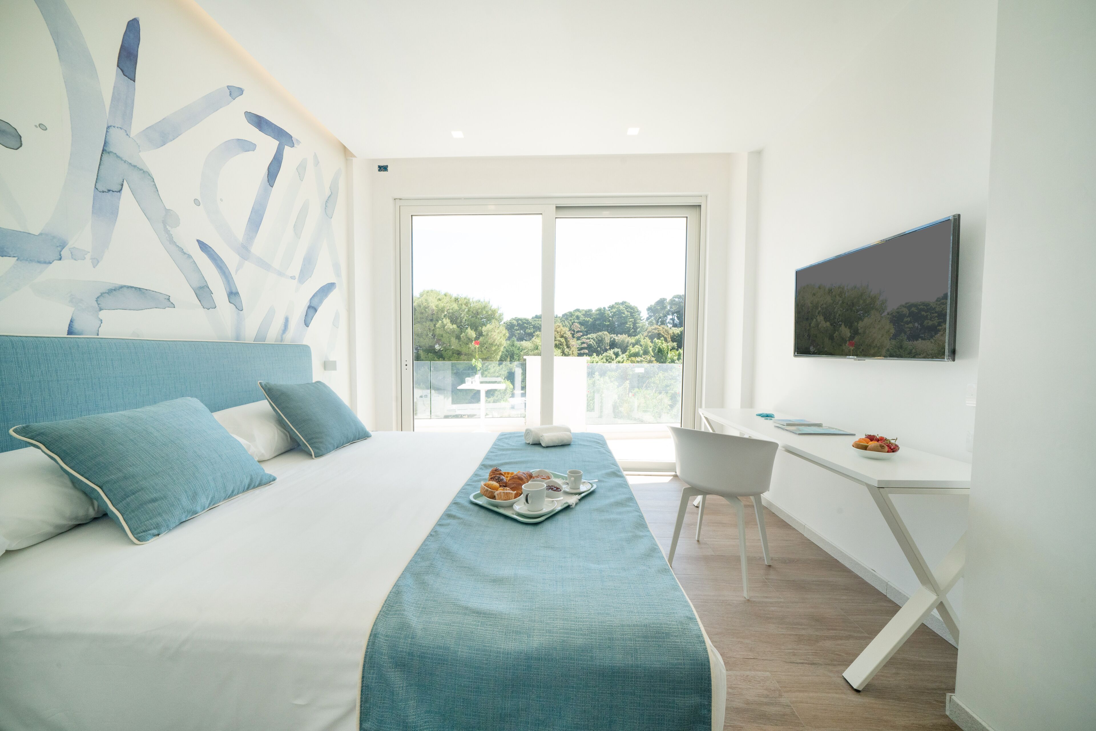 A modern hotel room with a large bed, a desk, and a view of the outdoors.