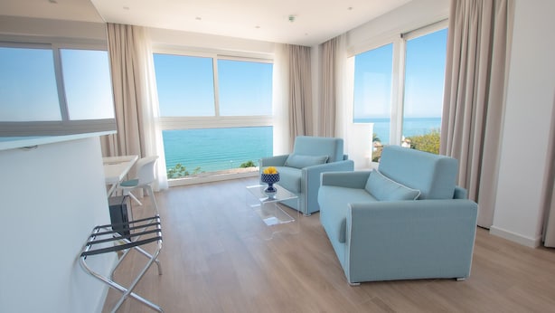A modern living room with a view of the sea, a dining area, and a balcony with a table and chairs. - Rodi Resort (Rodi Garganico)