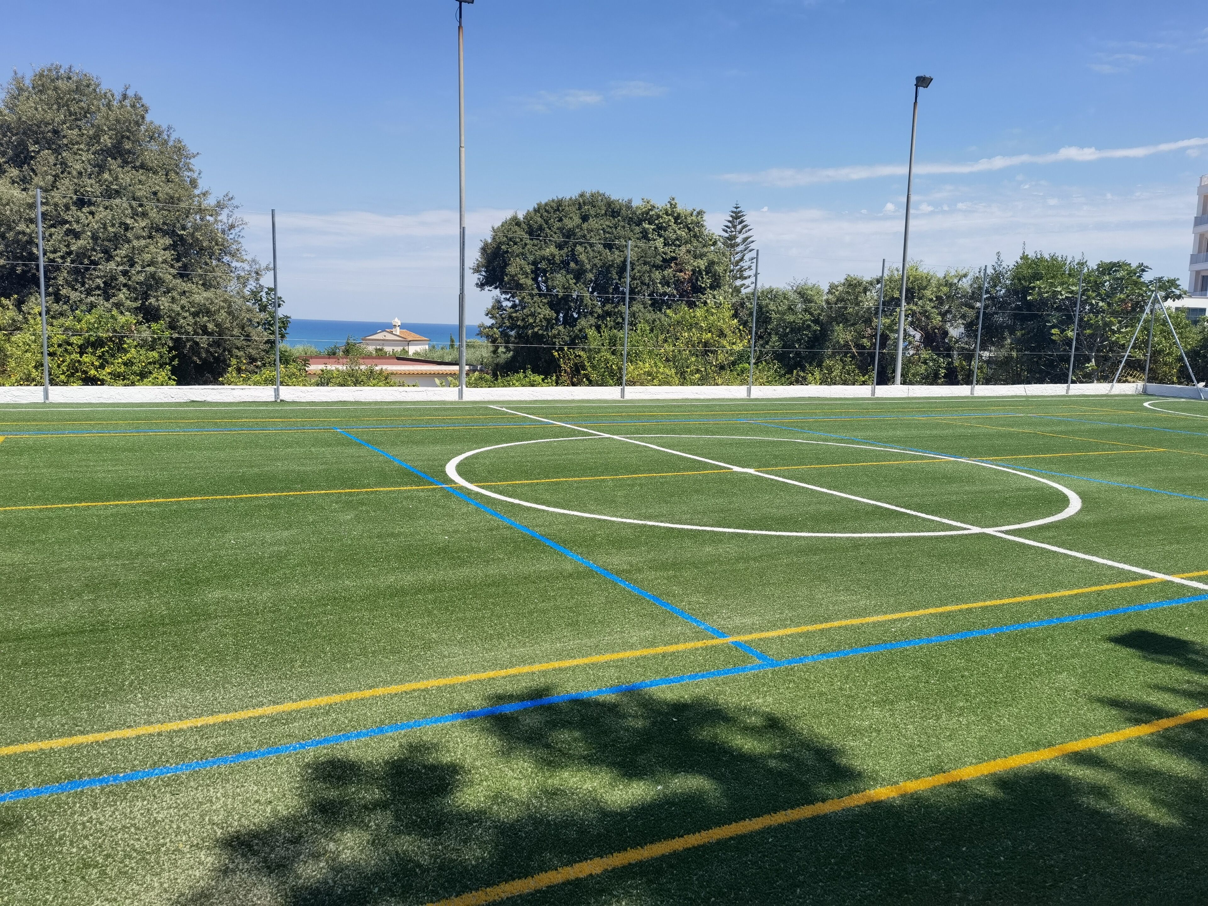 Un campo de fútbol con postes de portería, líneas marcadas y árboles al fondo.