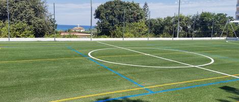 Un campo de fútbol con postes de portería, líneas marcadas y árboles al fondo.