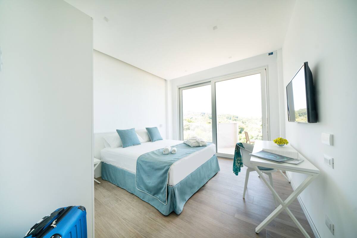 A modern hotel room with a bed, a desk, and a large window.