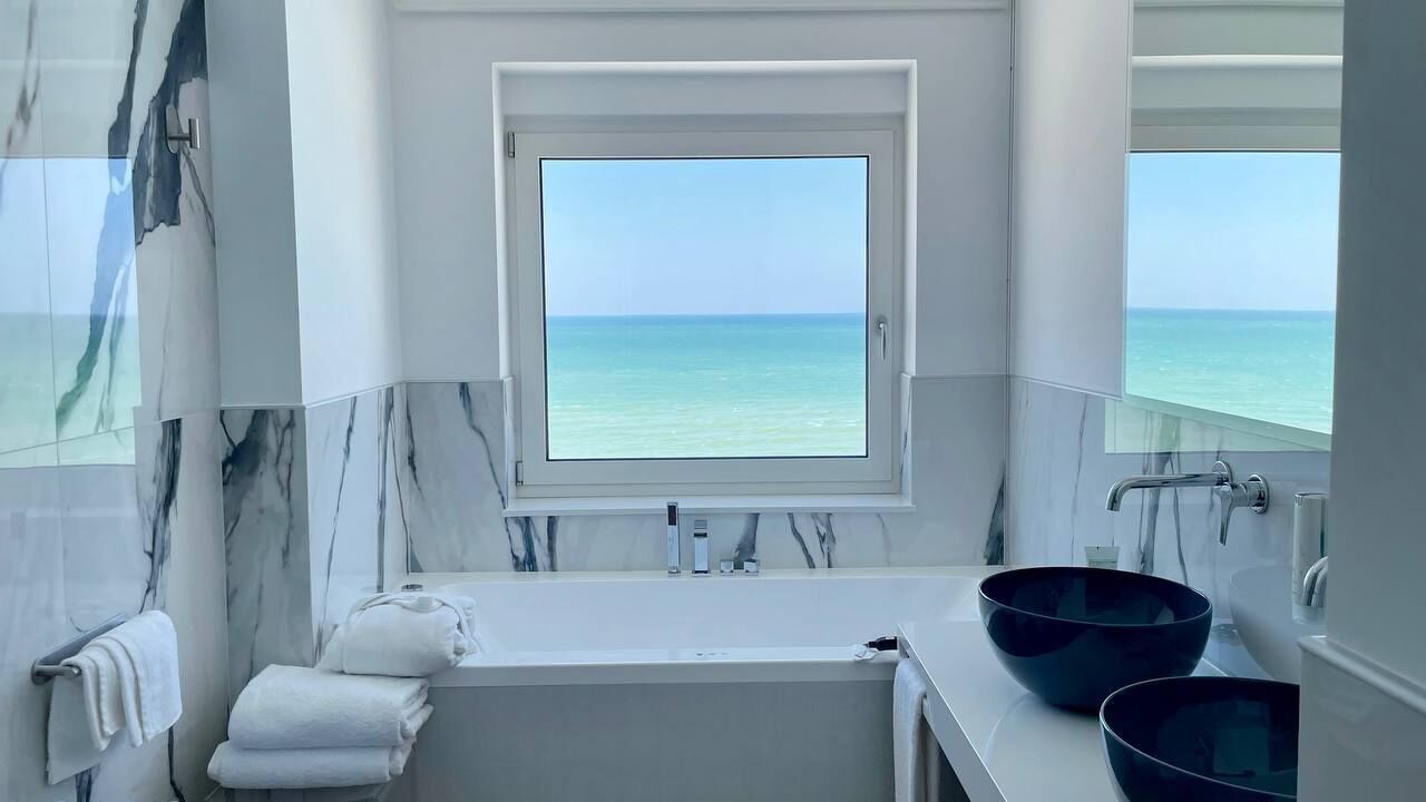 A bathroom with a large window, a bathtub, and two bowls on the counter.