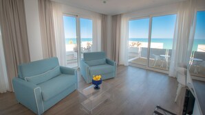A modern hotel room with a large balcony, two light blue armchairs, a clear glass table, and a vase with yellow flowers. - Rodi Resort (Rodi Garganico)