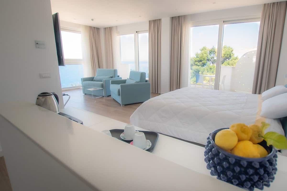 A hotel room with a large bed, a seating area with chairs, a coffee maker, and a fruit bowl on the windowsill.